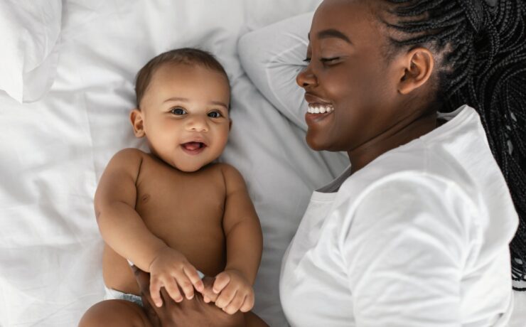 African American mom lying in bed with her laughing baby