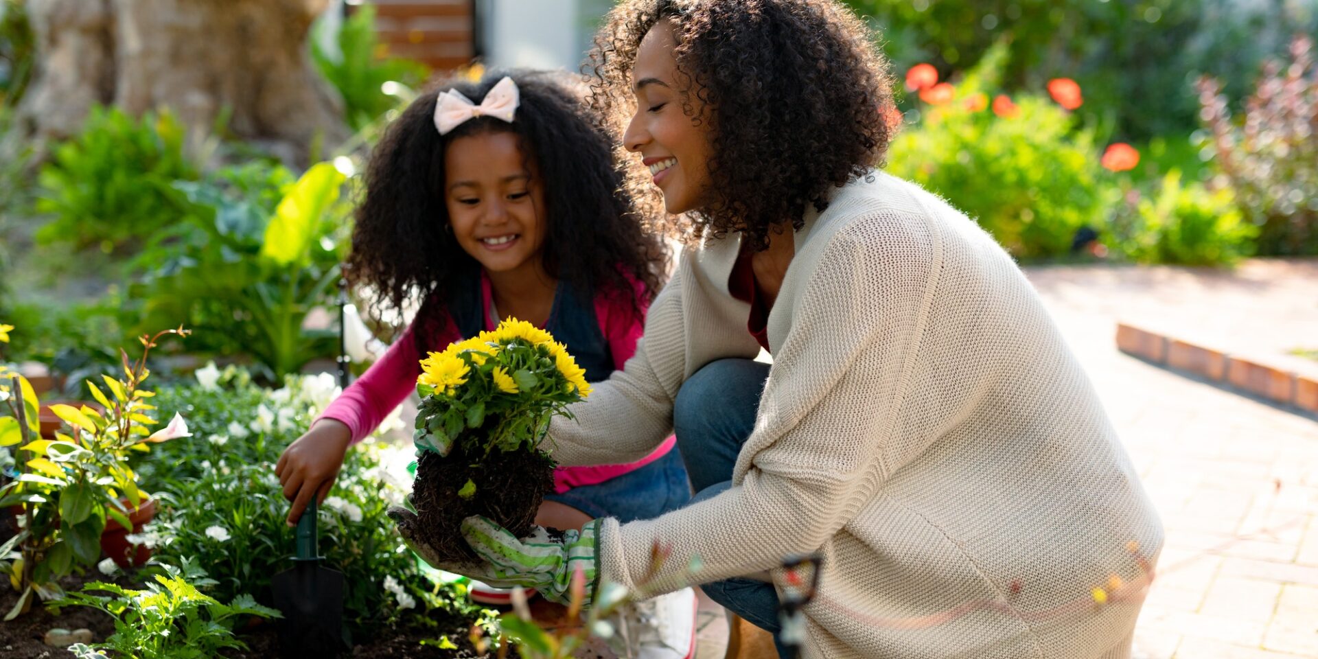 Happy african american mother and daughter planting flowers