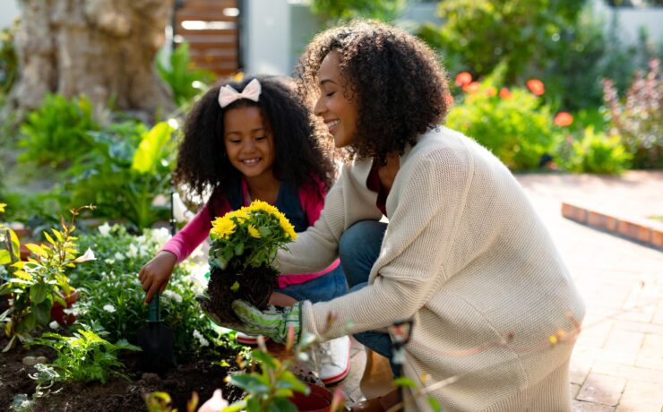 Happy african american mother and daughter planting flowers
